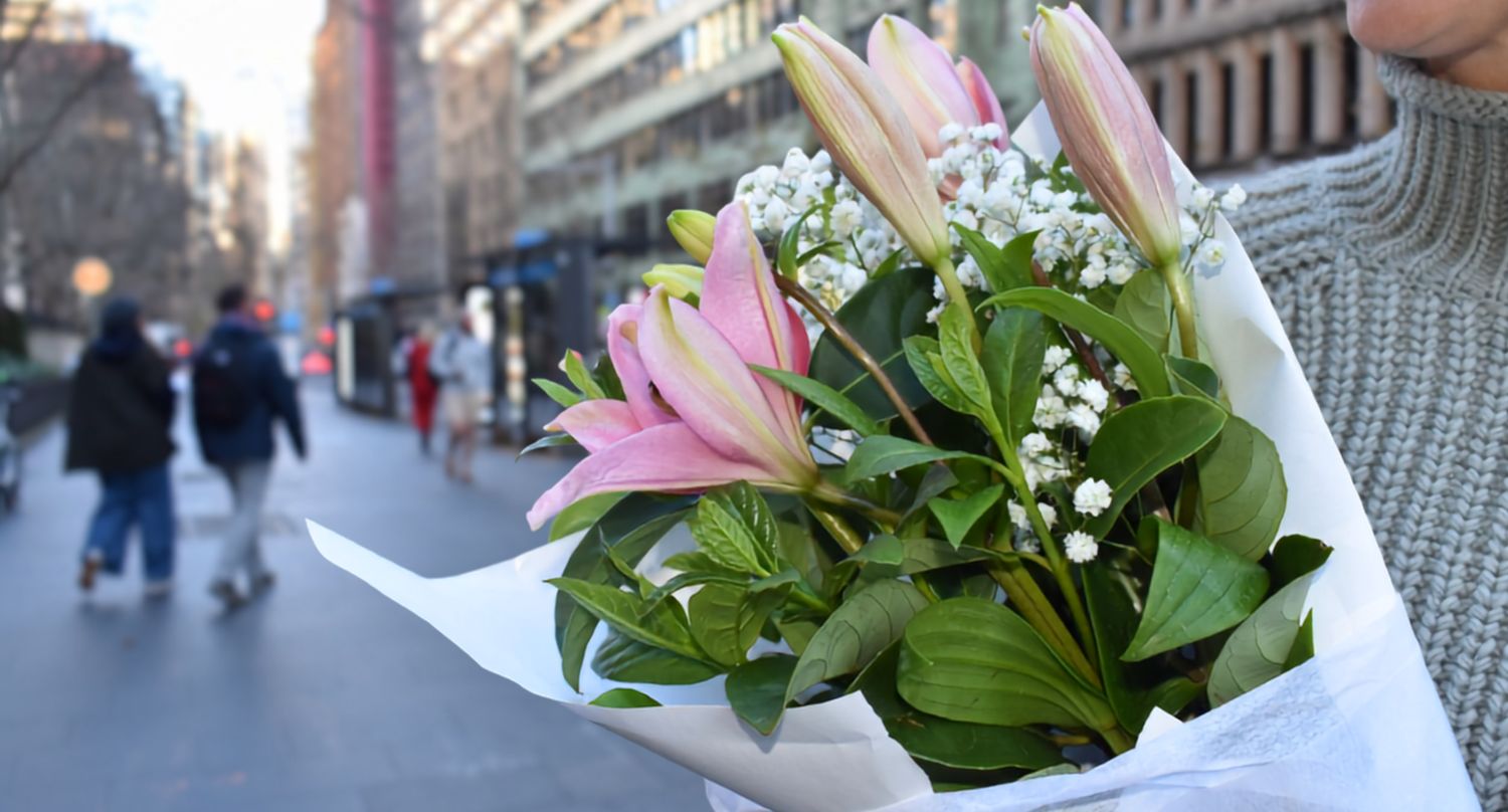 Close-up of the Lily Love Bouquet, with pink LA lilies, white gypsophila and green viburnum foliage wrapped in white paper.